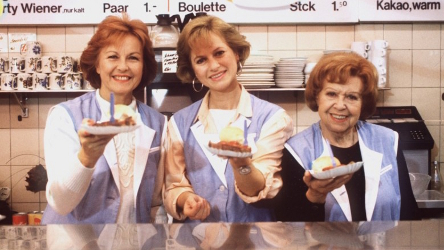 Drei Damen halten hinter einer Imbisstheke Pappschalen mit Currywurst in die Kamera